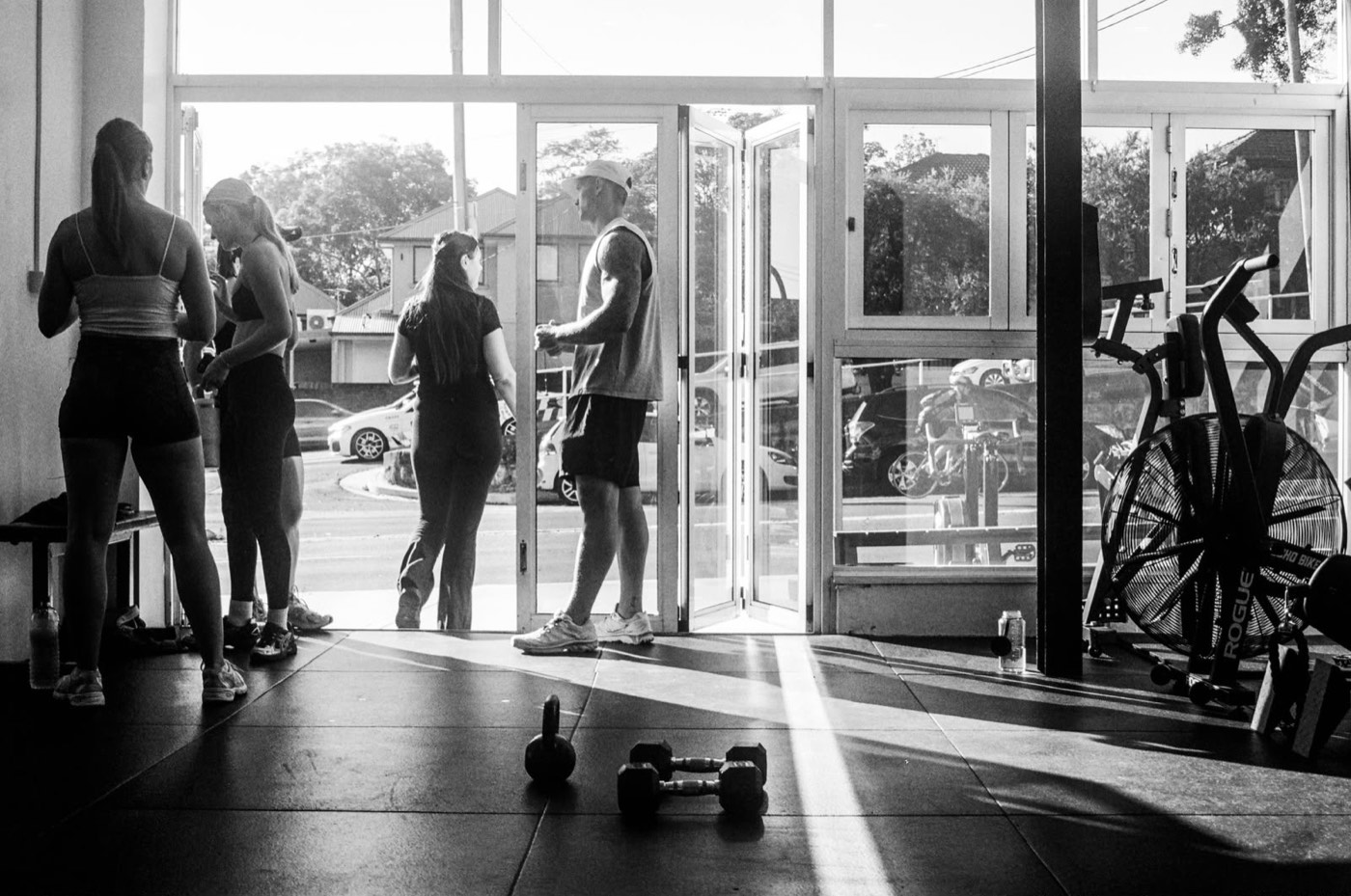 Members at the open studio door in morning light, kettlebell and dumbbells in the foreground
