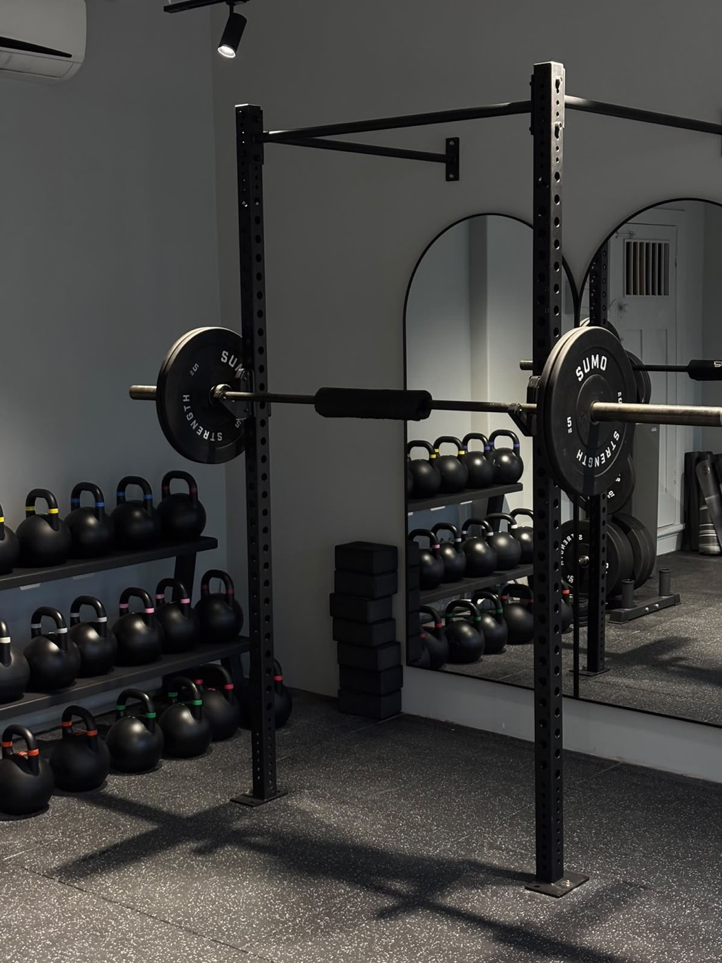 Kettlebell racks and a loaded barbell in front of the arched mirror